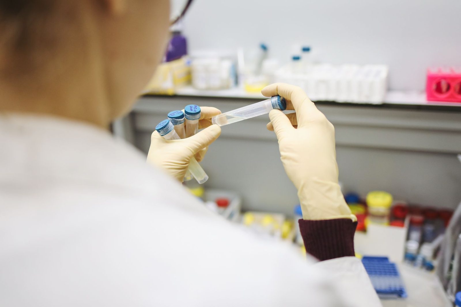 Osoba w fartuchu laboratoryjnym ogląda probówki z przezroczystą cieczą.
